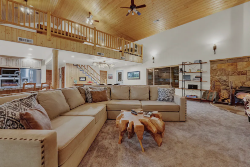 Cozy living room with a large sectional sofa, wooden accents, and a stone fireplace under a high ceiling.